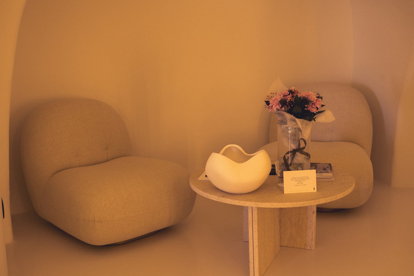 Two beige armchairs surround a stone table with fresh flowers.