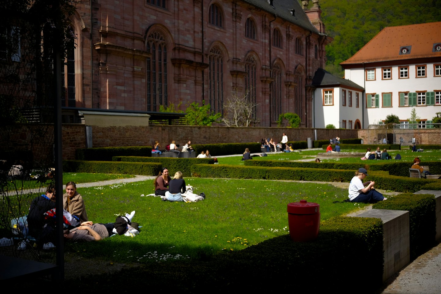 Young adults relax on a sunny green lawn in a garden courtyard.