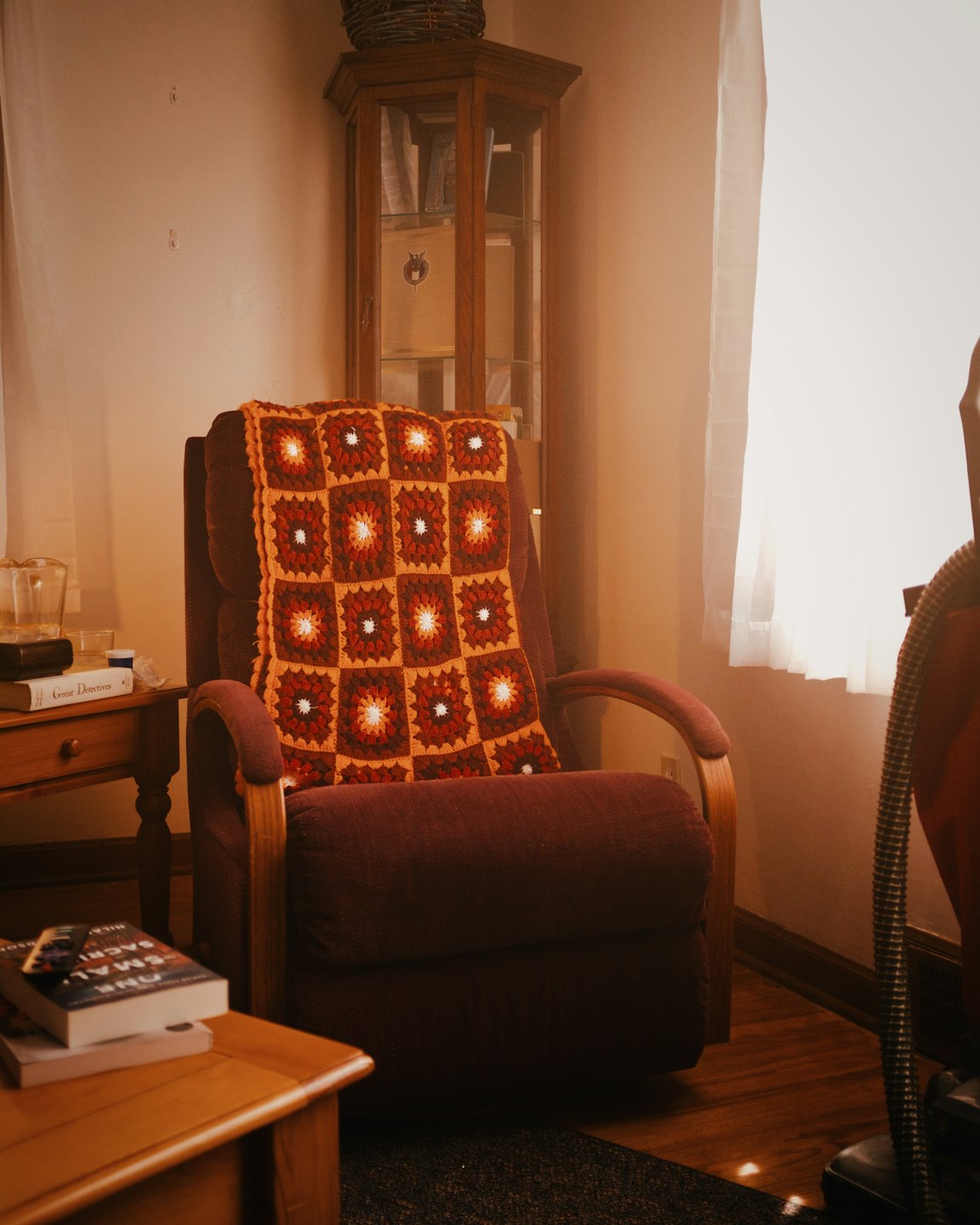 Maroon armchair draped with a colorful crocheted blanket.